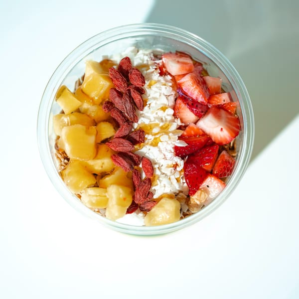 Overhead view of a smoothie bowl with pineapple, goji berries, coconut flakes, and strawberries.