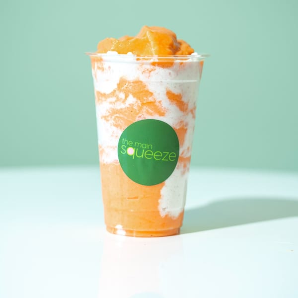 A vibrant orange and white swirled smoothie from The Main Squeeze, topped with fruit chunks.