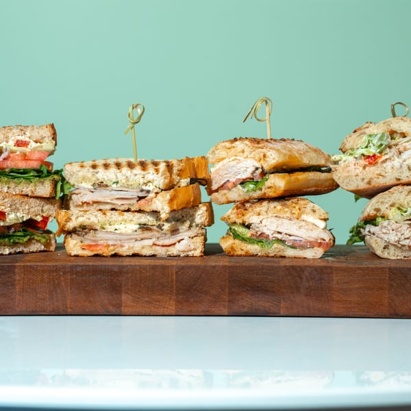 Assortment of sandwiches, including grilled paninis and deli sandwiches, on a wooden cutting board.