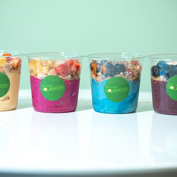 Four colorful smoothie bowls from The Main Squeeze, topped with granola and fresh fruit.