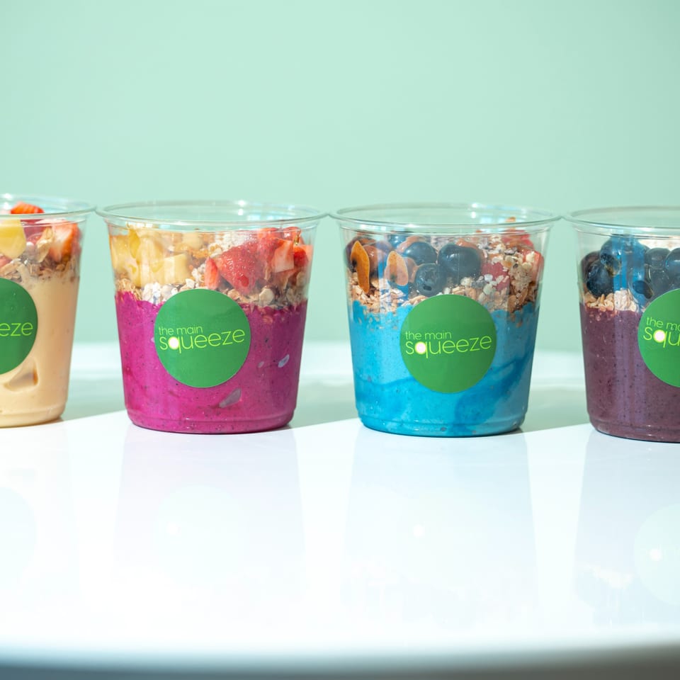 Four colorful smoothie bowls from The Main Squeeze, topped with granola and fresh fruit.