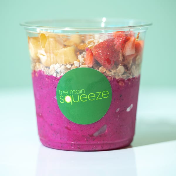 A vibrant pink smoothie bowl from The Main Squeeze, topped with granola, strawberries, and bananas.